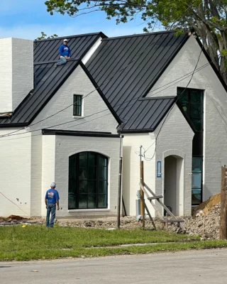 Workers installing a metal roof on a newly constructed house.