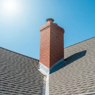 Well-maintained roof with shingles and chimney under a clear blue sky